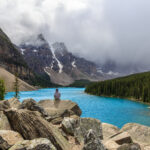 A lone girl sits on a pile of rocks overlooking Moraine Lake in Banff National Park